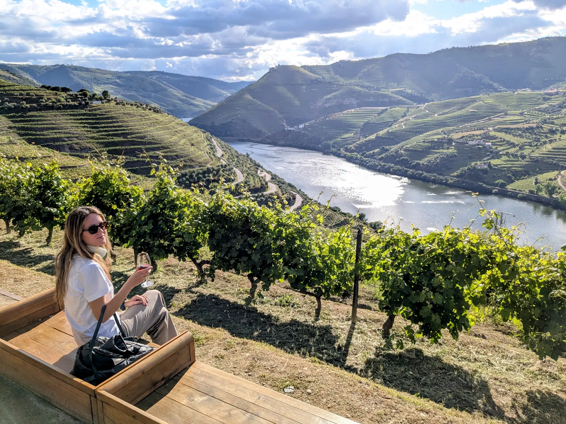 A traveler holding a glass of port wine above the terraced vineyards and river of the Douro Valley