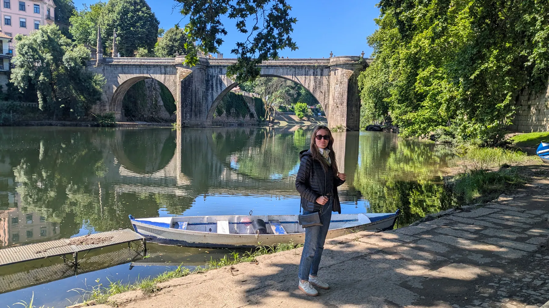 A traveler standing beside a boat and old stone bridge by the river in Amarante