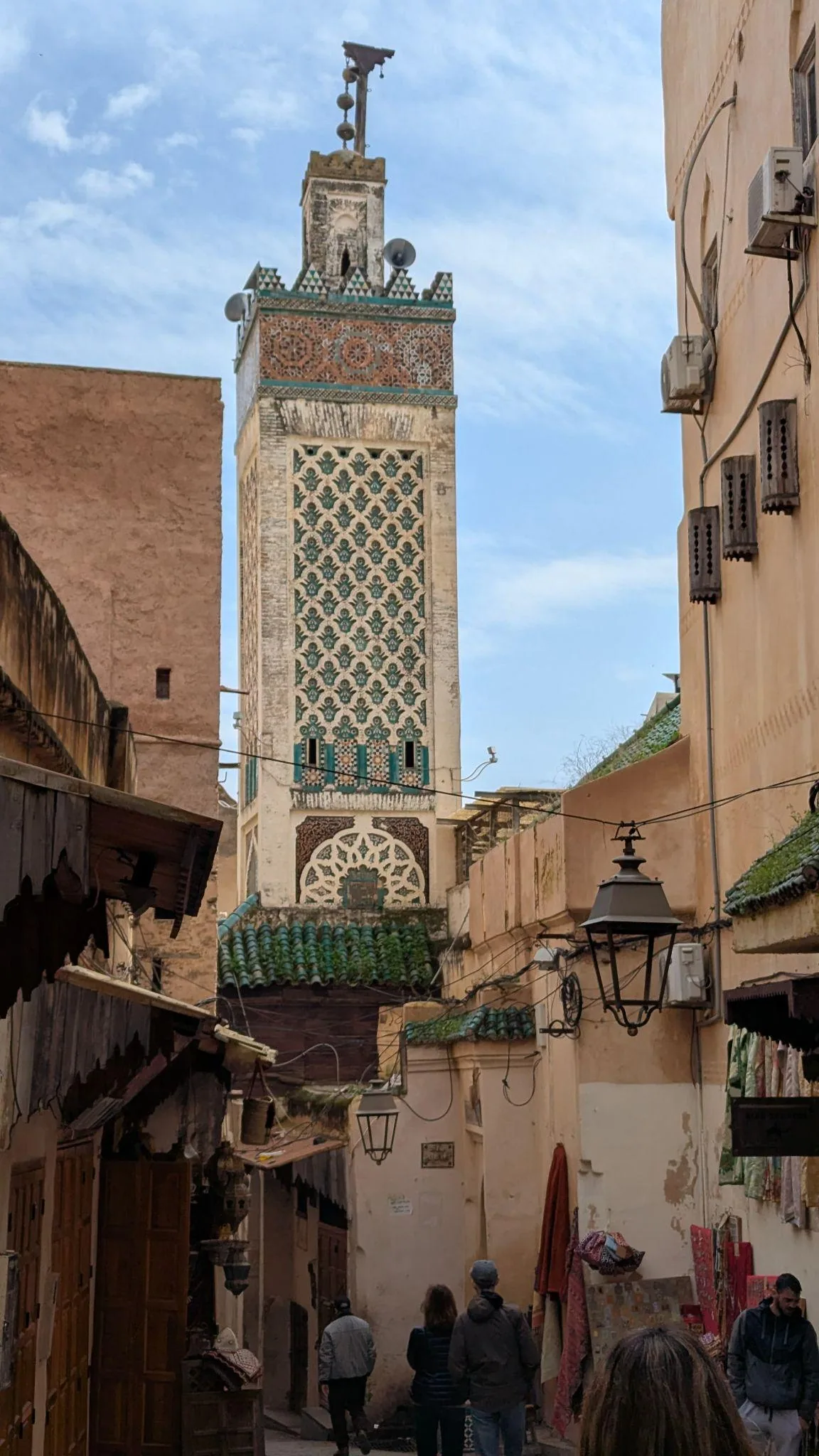 A narrow Fez medina street with a minaret rising above the rooftops