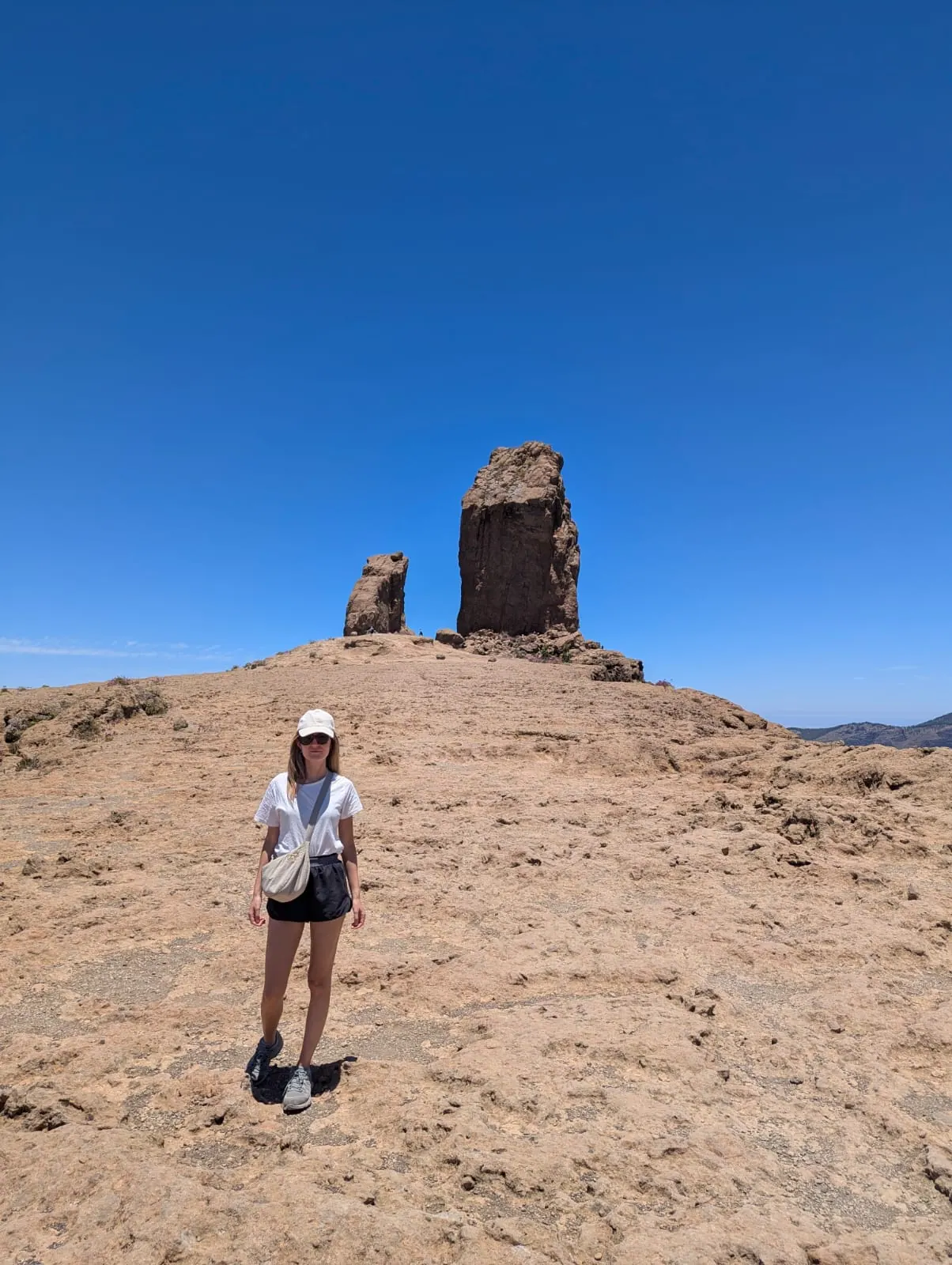 A traveller standing beside the Roque Nublo monolith under a clear blue sky