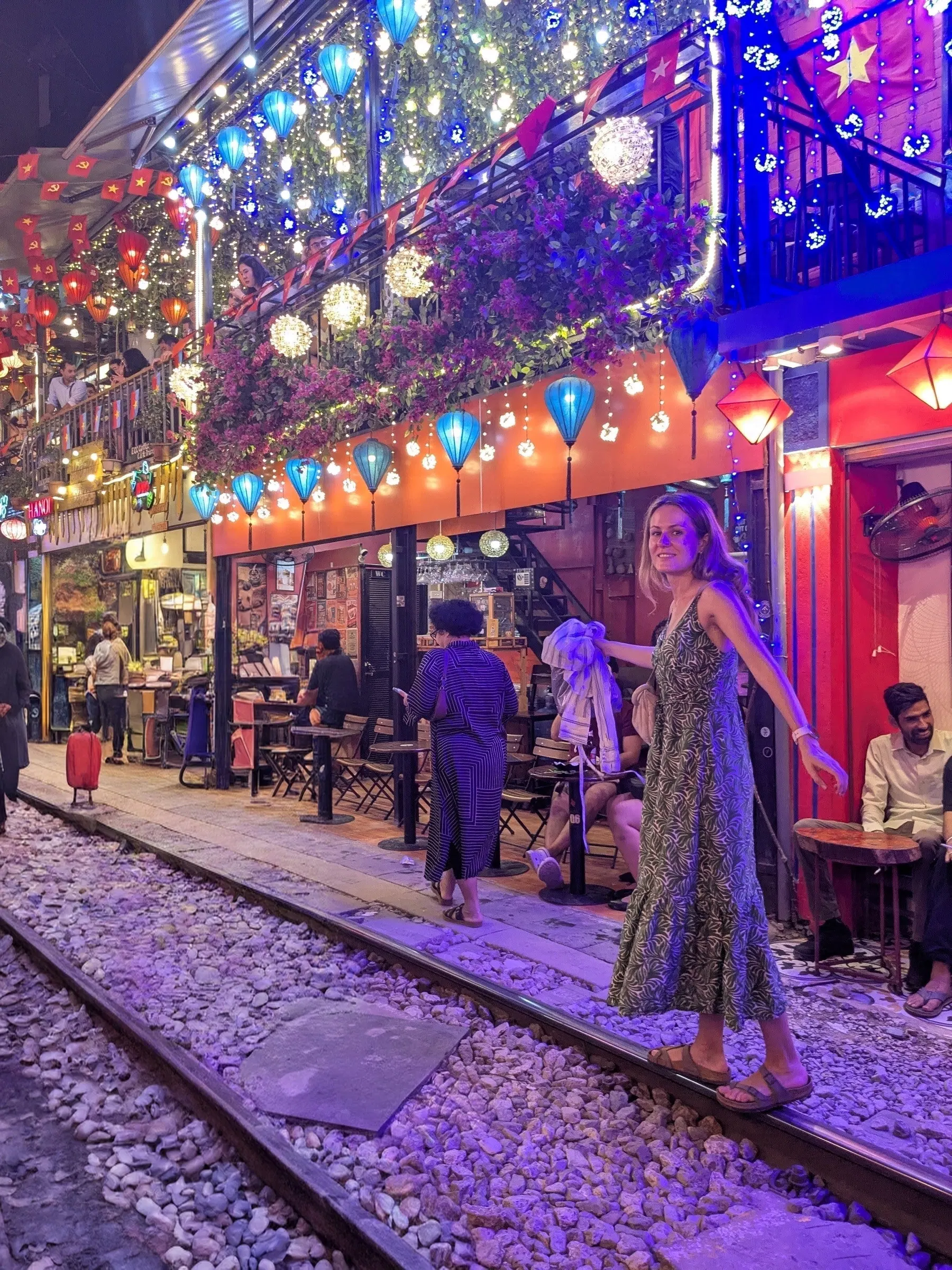 Bright overhead lanterns and illuminated cafes lining the narrow tracks of Hanoi Train Street at night