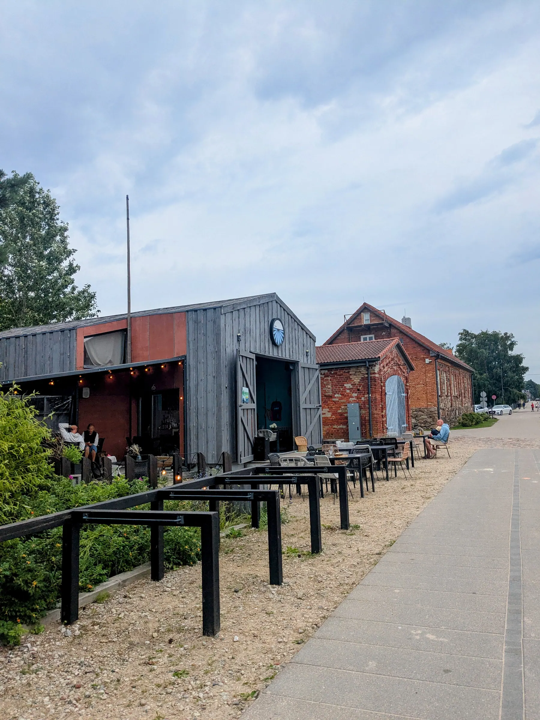 Outdoor café tables beside restored wooden and brick buildings in Pāvilosta
