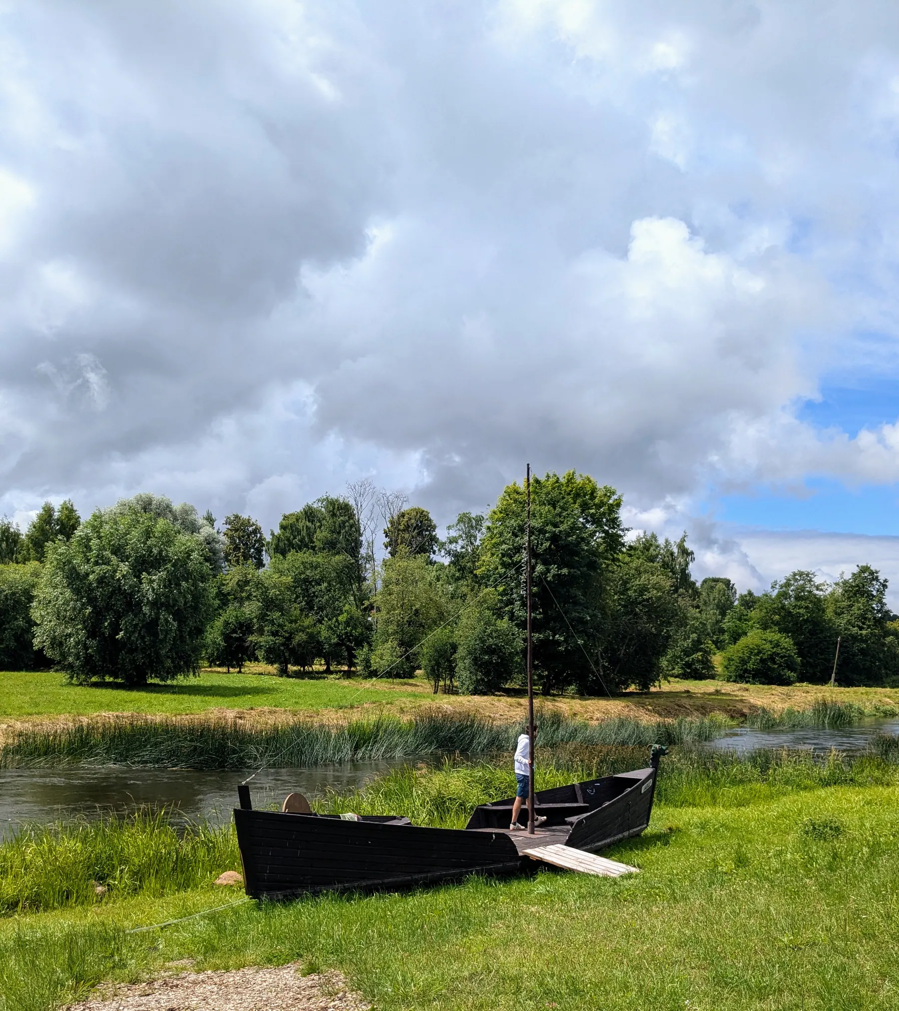 An old black wooden boat on the grassy bank of the Abava River in Sabile