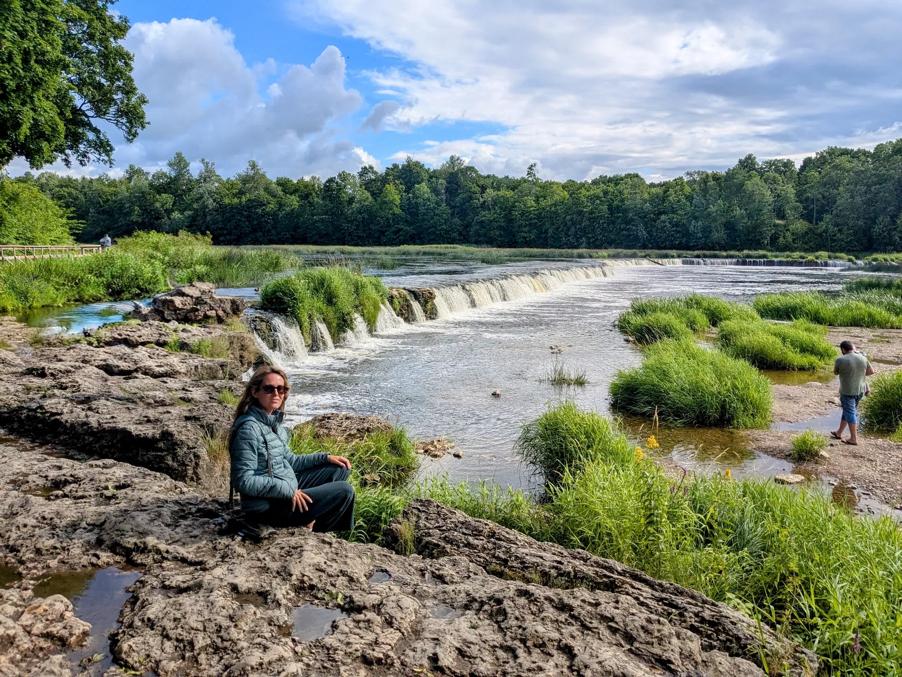 A traveler beside the wide Ventas Rumba waterfall in Kuldīga