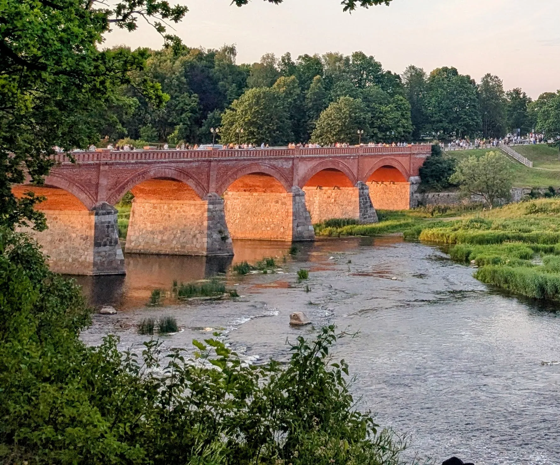 Kuldīga's historic brick bridge glowing above the Venta River