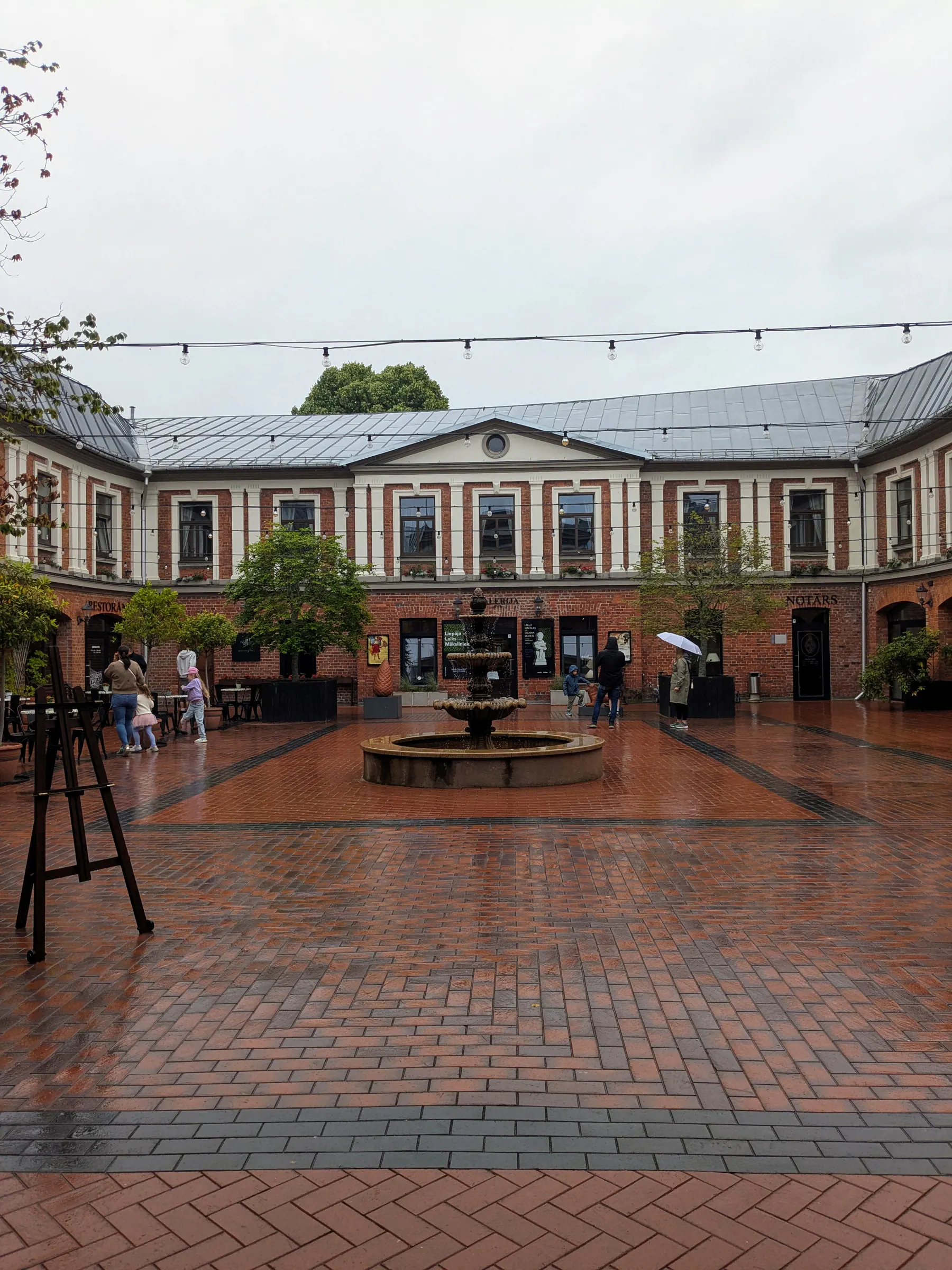 The brick courtyard of Galerija Romas dārzs on a rainy day