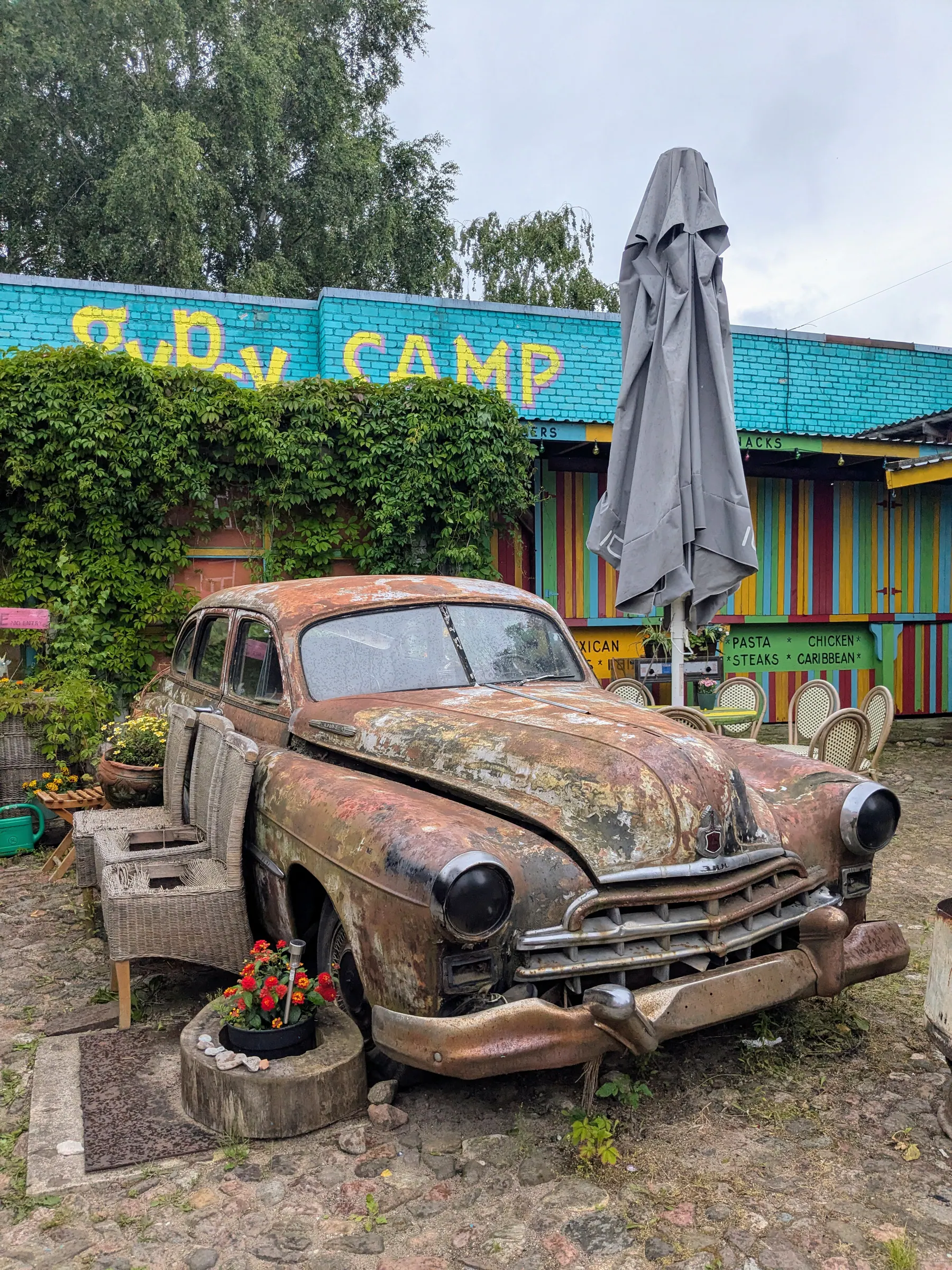 A rusted vintage car covered with plants in the Gipsy Camp courtyard