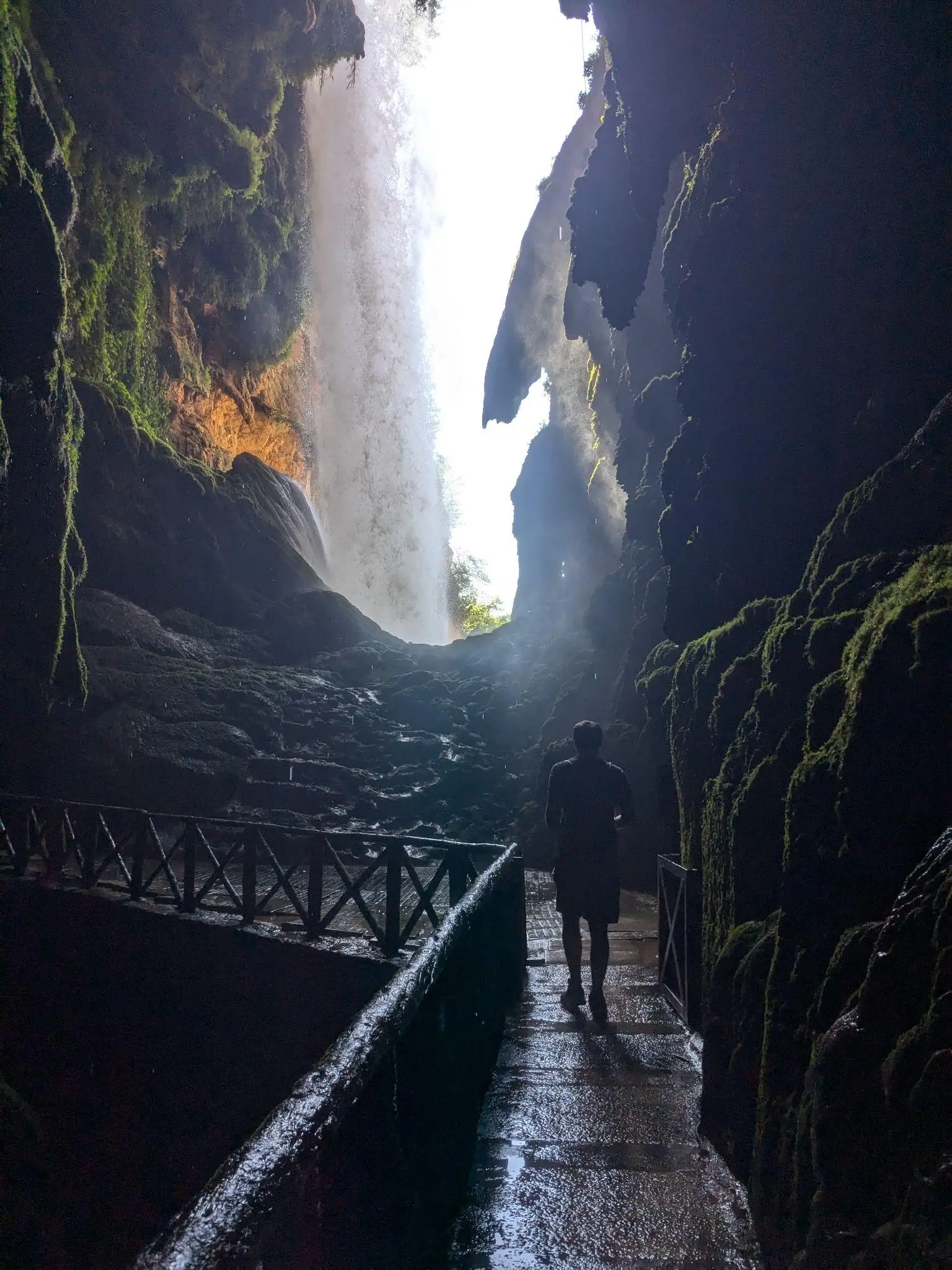 A person walking through the dark Iris Grotto behind the waterfall