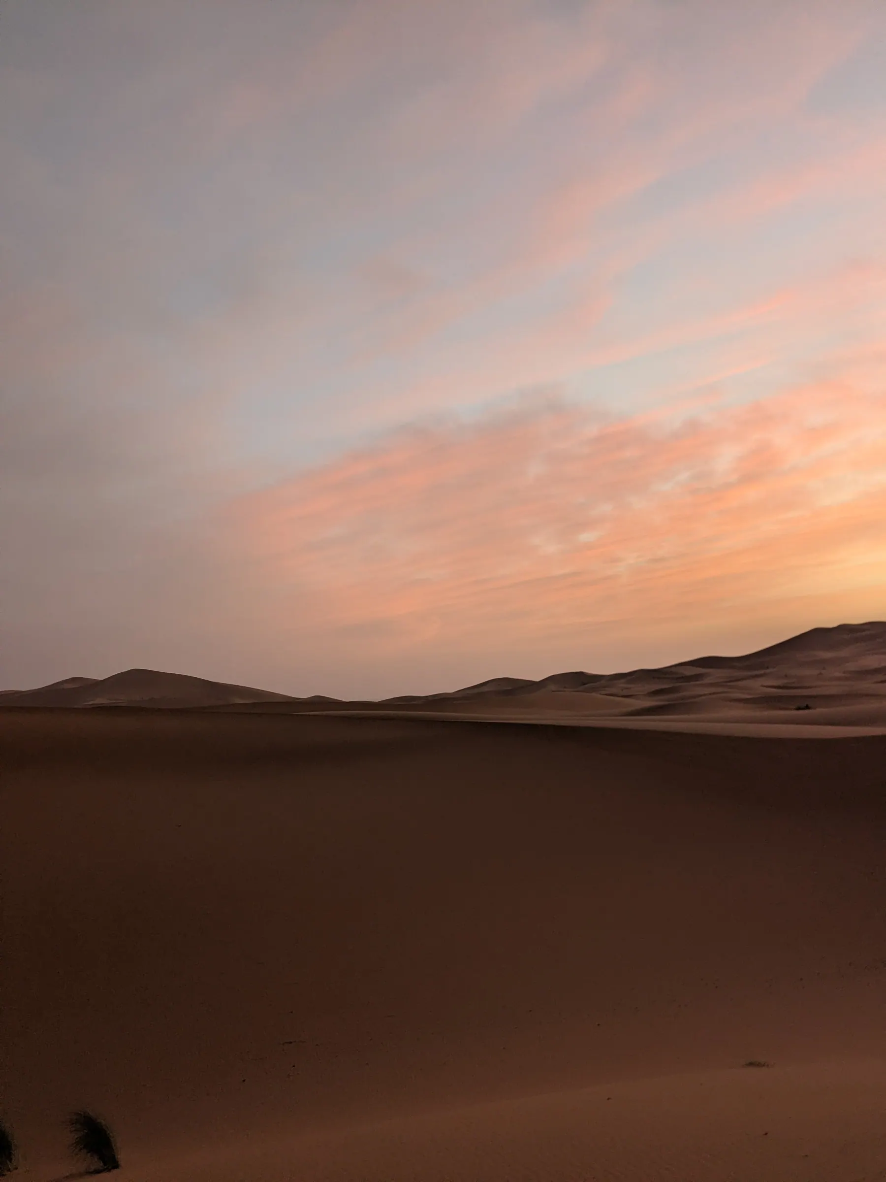 Pink sunrise clouds above Sahara dunes in Morocco