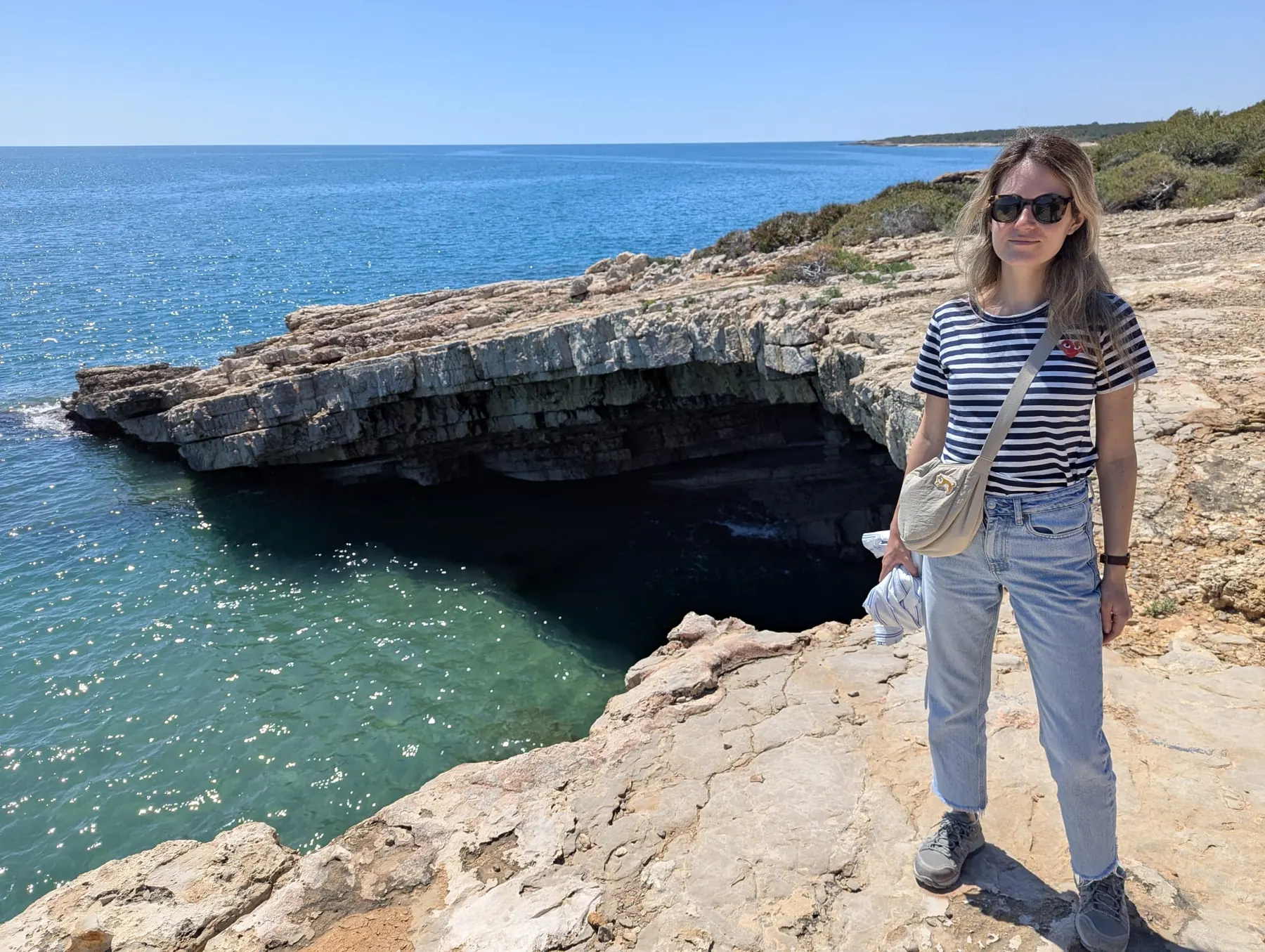 A traveler standing beside a sea cave on the rocky coast near Cala Ordi