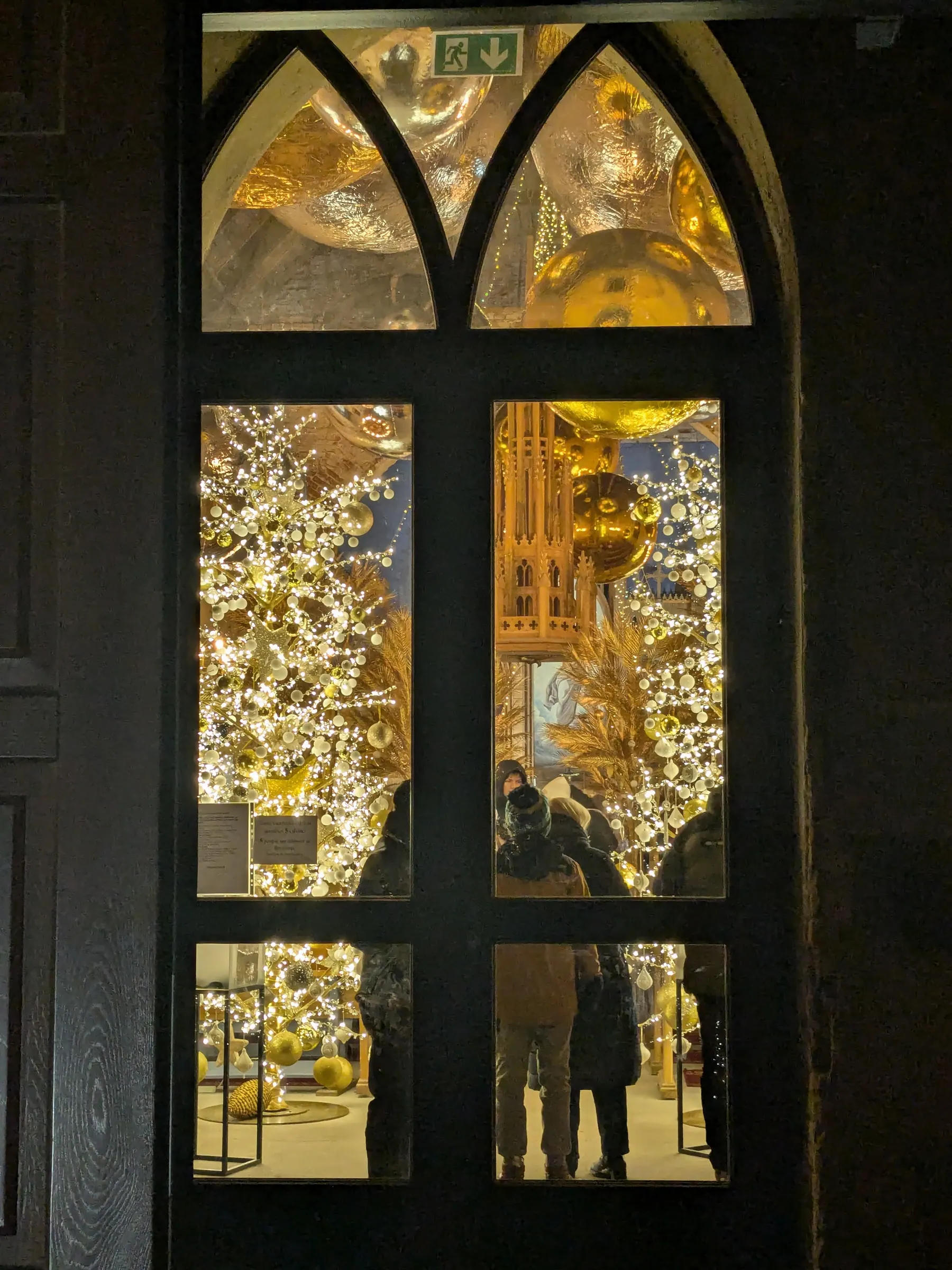 Gothic arched window of Ropaži Church looking from winter dusk into the warm golden illuminated interior