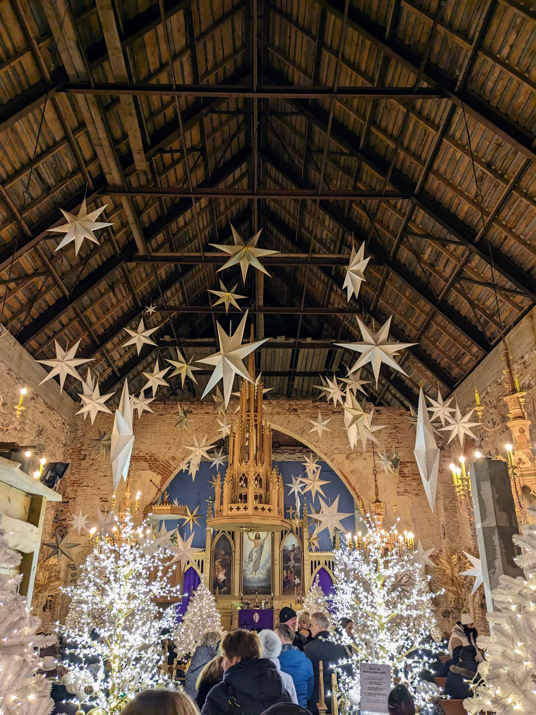 The nave of Ropaži Church looking toward the wooden altar beneath soaring timber rafters hung with illuminated 3D stars