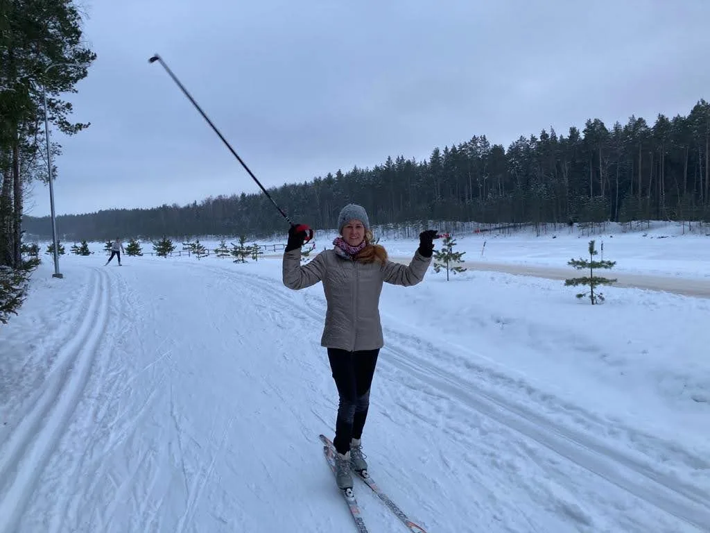 The author smiling on cross-country skis with poles raised along a snow-covered forest trail in Latvia