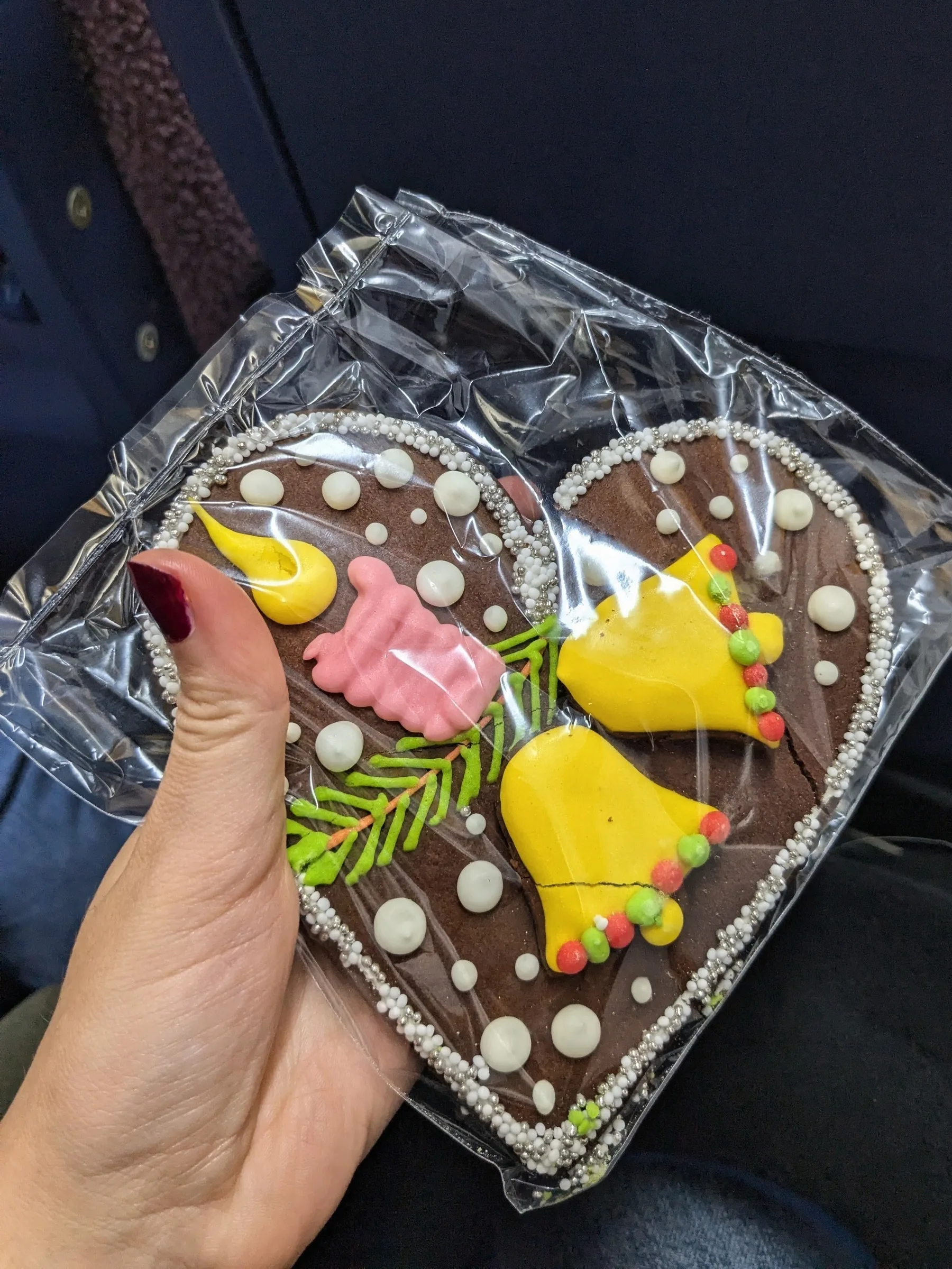 A hand holding a heart-shaped traditional Latvian piparkūka gingerbread cookie elaborately decorated with colorful royal icing and bells