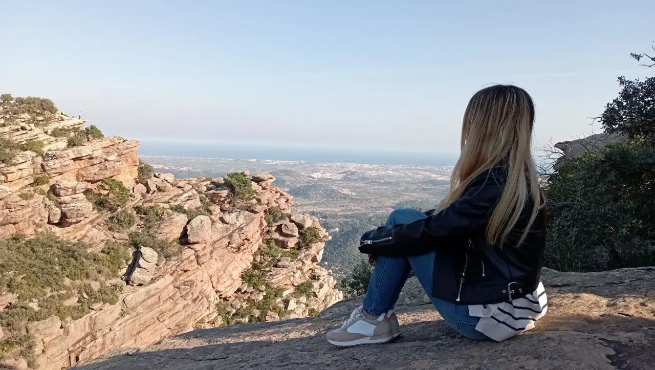 A traveler sitting on the red sandstone edge at Mirador del Garbí