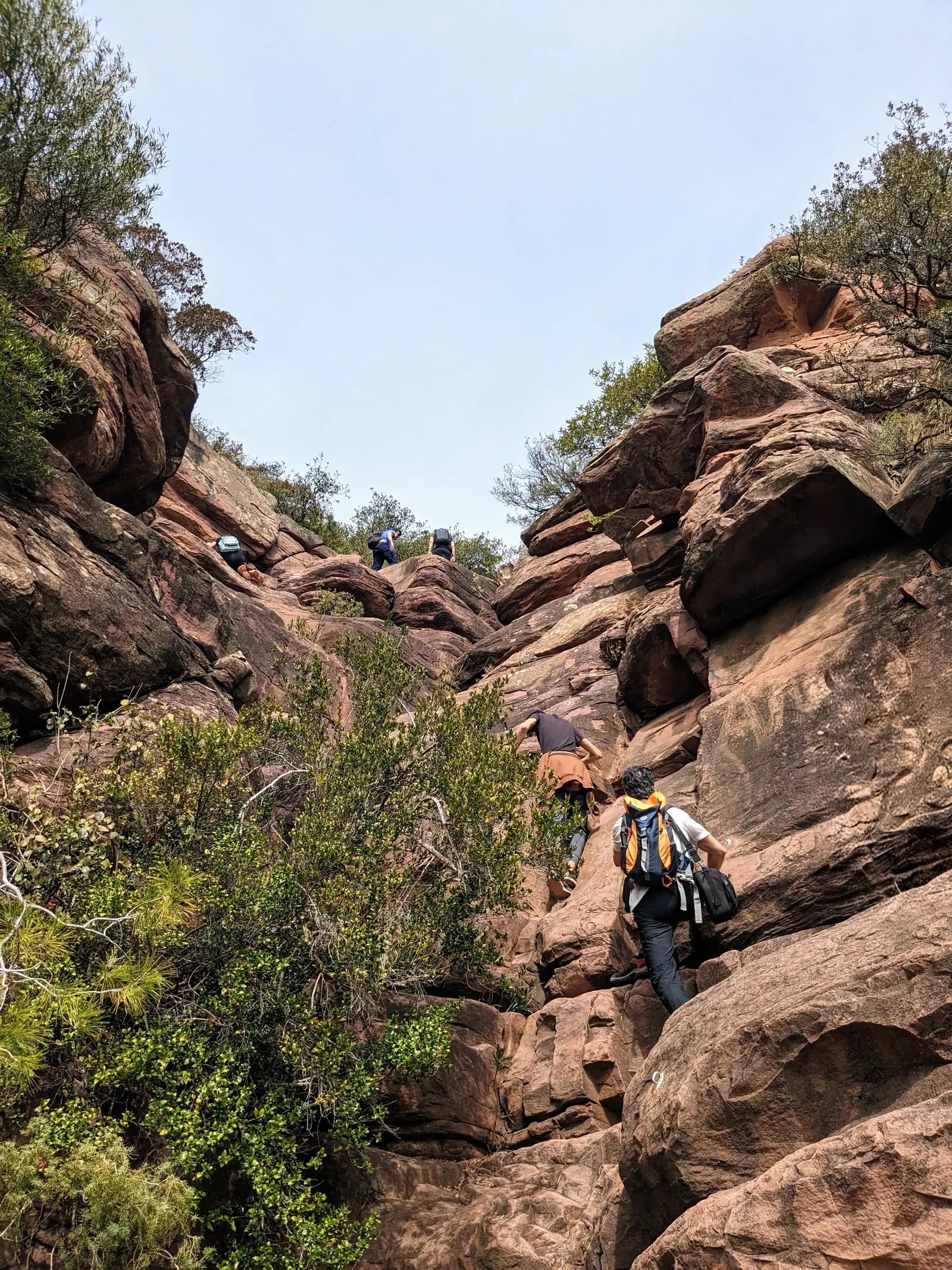 A hiker climbing through the red rock of the Ruta de les Cadenes