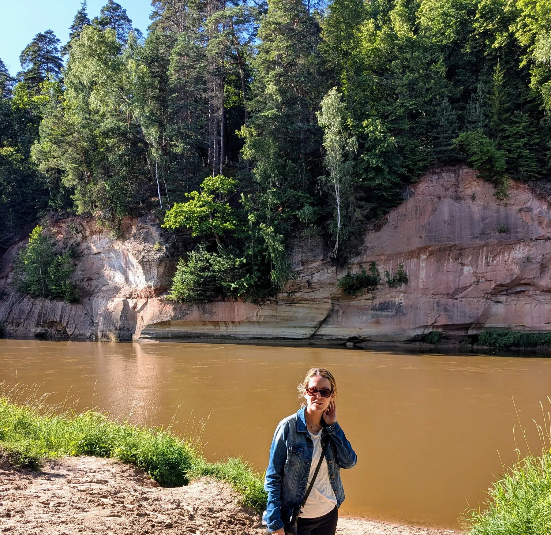 A traveler beside the Gauja River and red sandstone cliffs in Sigulda
