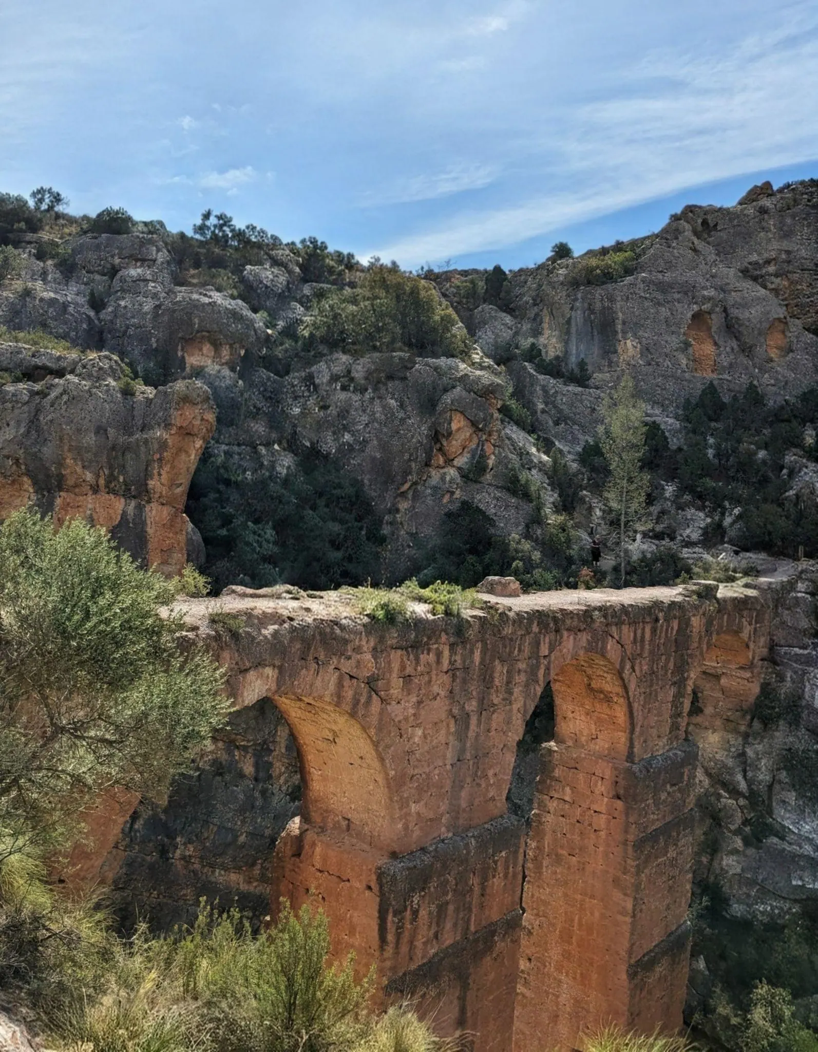 Stone arches of the Roman aqueduct bridge spanning high above the forested ravine near Chelva