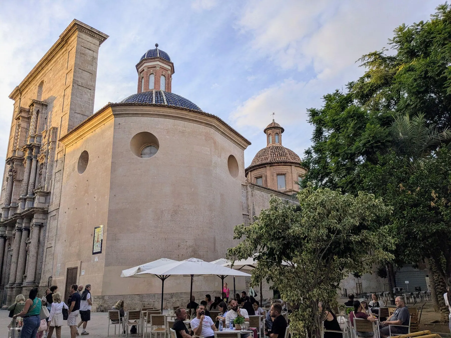 Cobbled square of Plaza del Carmen with church dome, shaded cafe terraces, and leafy trees