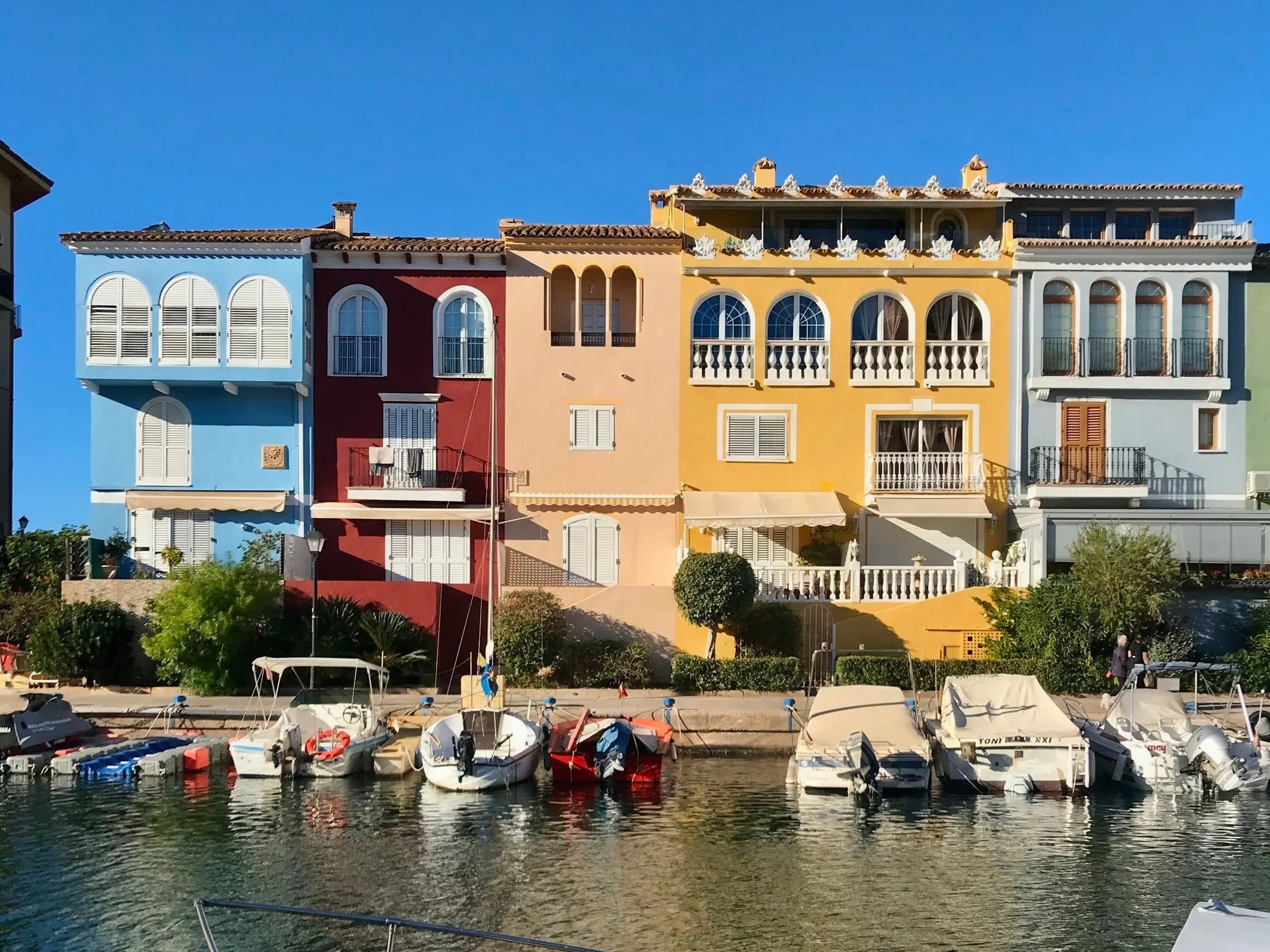 Row of colorful pastel waterfront townhouses and moored leisure boats along the canal marina in Port Saplaya